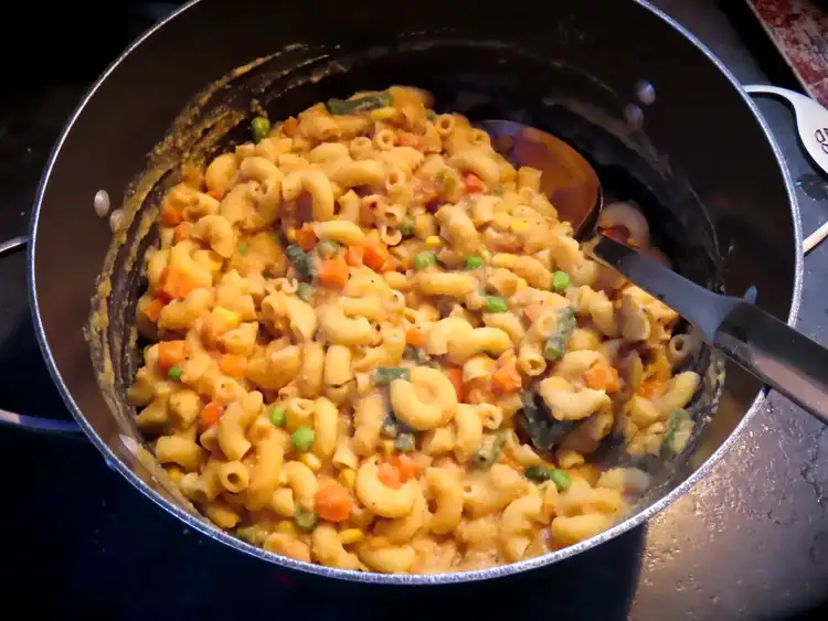 A pot of macaroni pasta with thick, creamy, cheesy (vegan) sauce mixed with peas, carrots, and green beans.